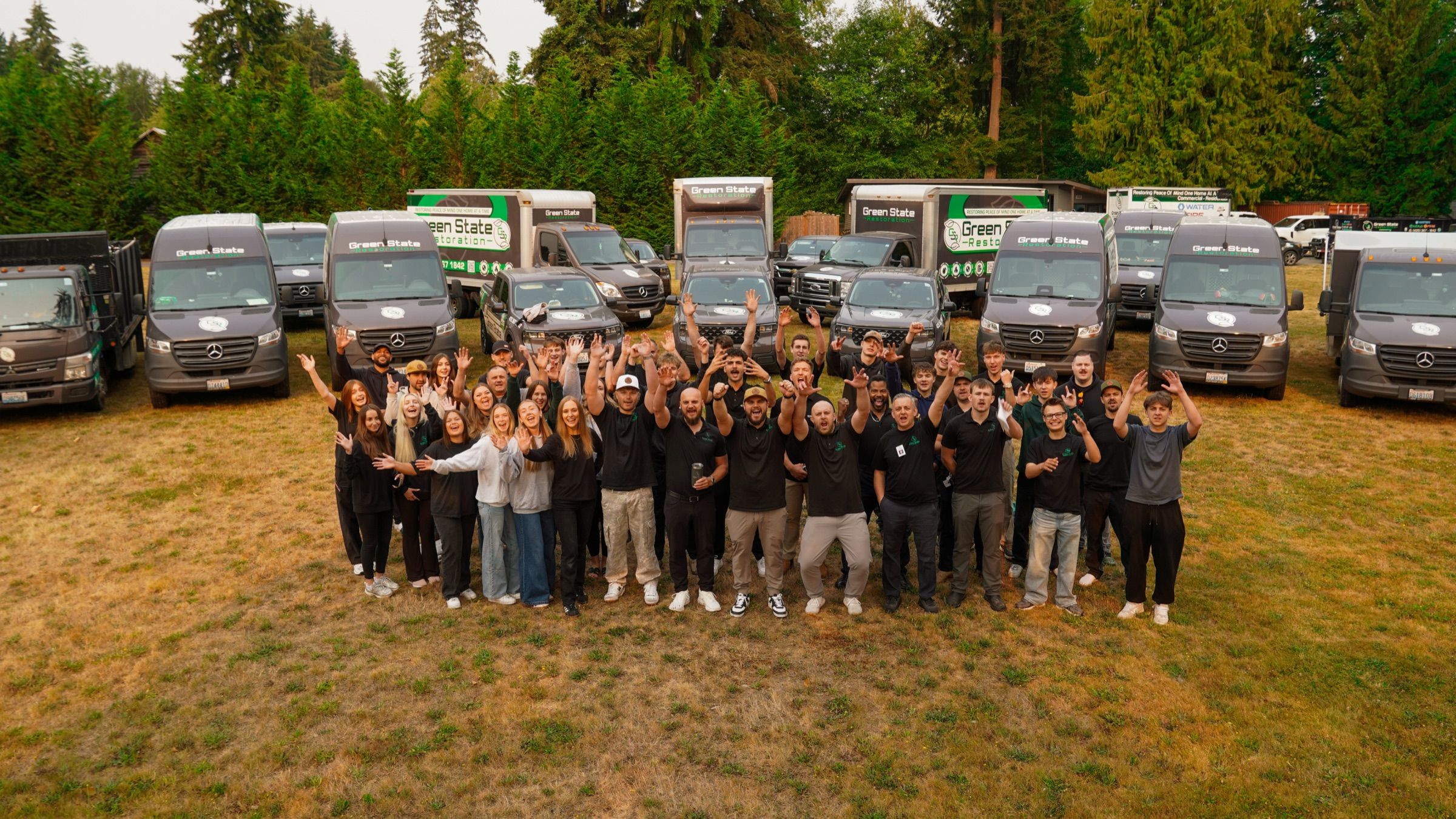 Green State Restoration full company team cheering in front of branded restoration vehicles
